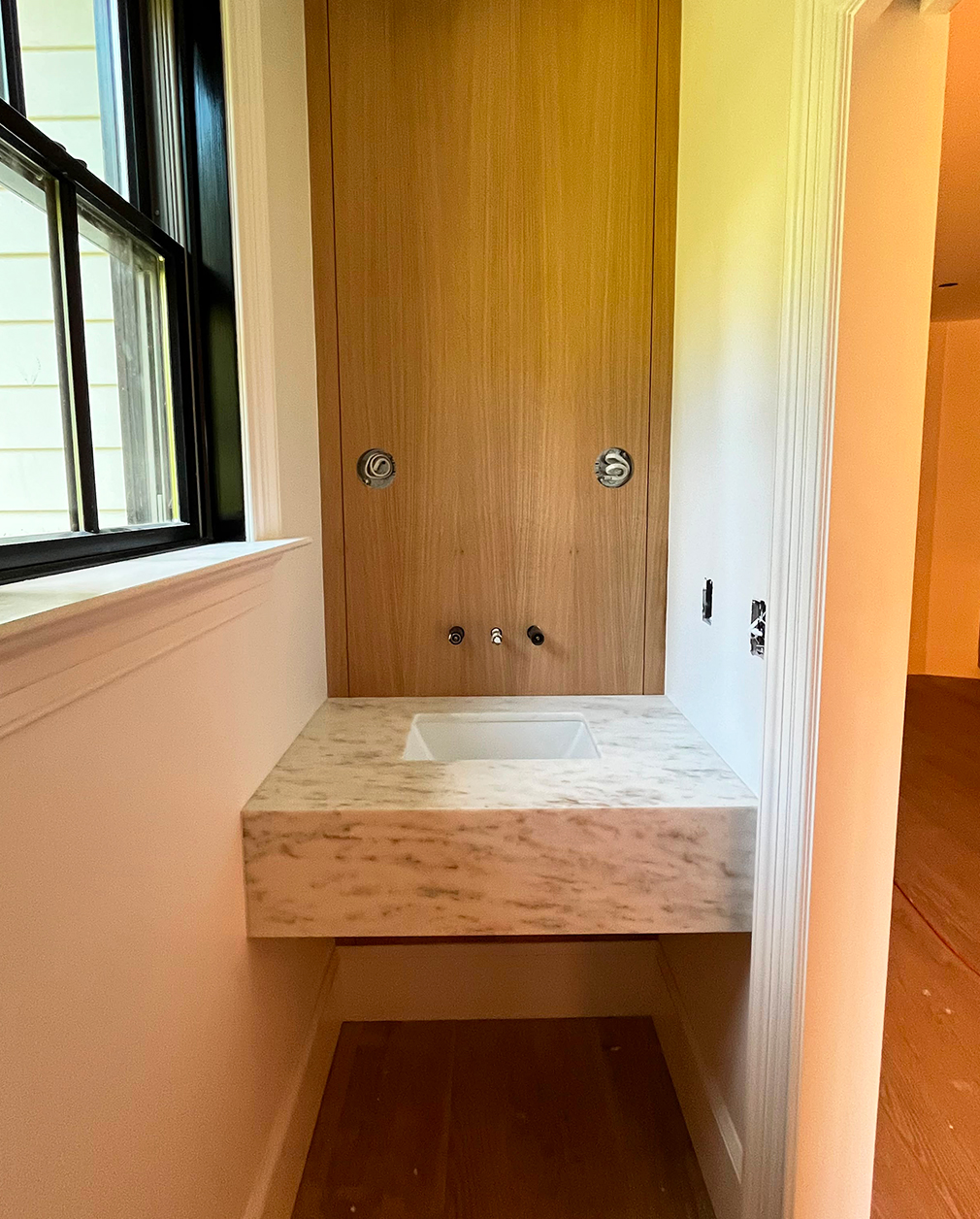 A floating marble vanity against white-oak paneling in a freshly finished powder room.