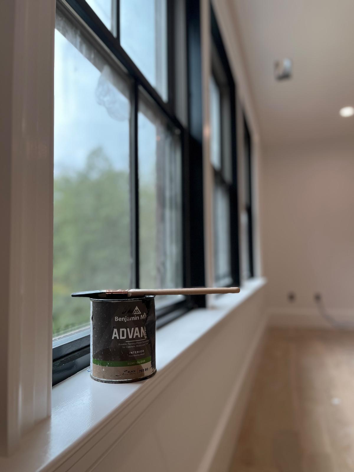 A quart of Benjamin Moore Advance semi-gloss resting on a windowsill beside freshly painted black sash windows.